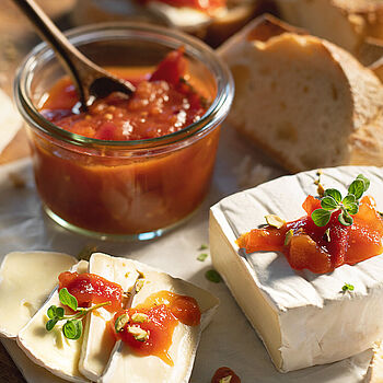 Kleine Portion Tomaten-Chutney im Glas, dazu ein Laib Géramont Käse und frisches Baguette