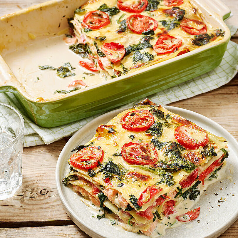 Spinat-Lachs-Lasagne, garniert mit frischen Kräutern und Tomaten. Serviert in einer grünen Auflaufform.