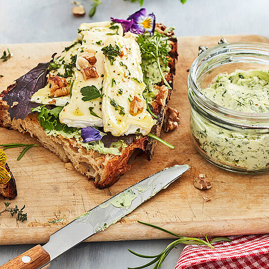 Frisches Sauerteigbrot mit Camembert von Le Rustique und Bärlauchbrutter auf einem klassischen Holzschneidebrett serviert