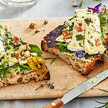 Frisches Sauerteigbrot mit Camembert von Le Rustique und Bärlauchbrutter auf einem klassischen Holzschneidebrett serviert