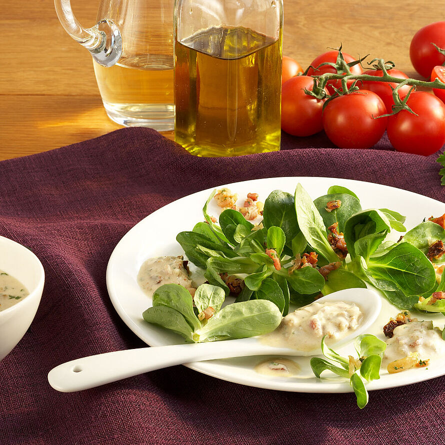 Frischer Feldsalat mit Speck und Pinienkernen auf einem Teller serviert. Dazu ein schmackhaftes Blauschimmeldressing