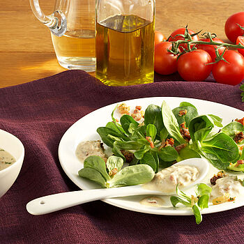 Frischer Feldsalat mit Speck und Pinienkernen auf einem Teller serviert. Dazu ein schmackhaftes Blauschimmeldressing
