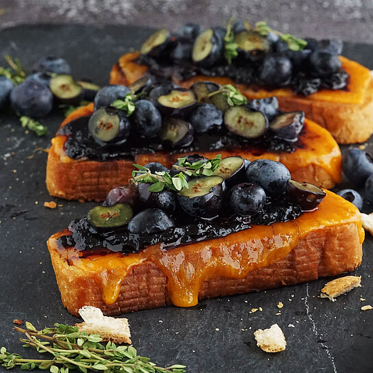 Knuspriges Stullen Rezept mit Cheddar und frischen Heidelbeeren, serviert mit Zitronenthymian auf einer schwarzen Schieferplatte.
