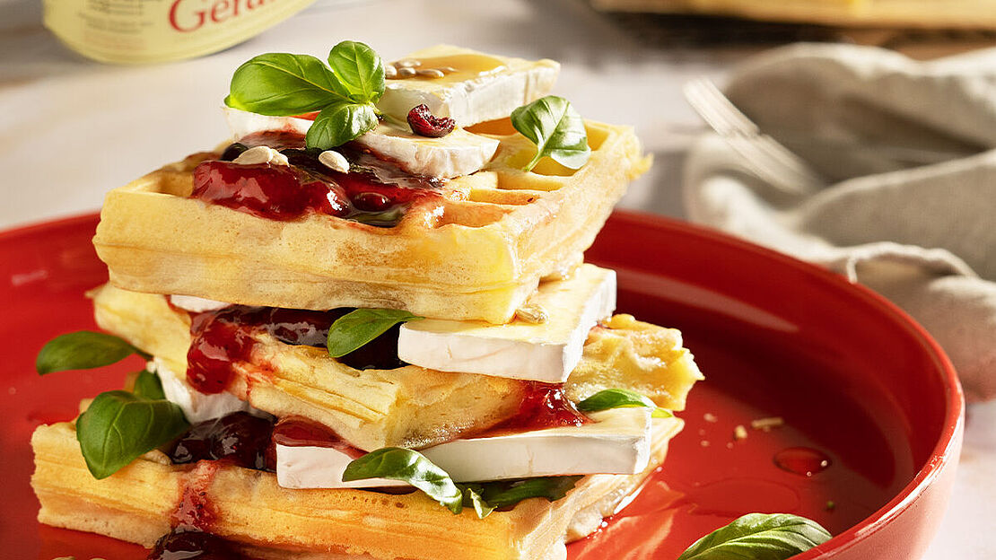 Herzhafte frische Waffeln mit Géramont, Cranberries und Preiselbeeren. Aufgetürmt angerichtet auf einer toten Platte. 