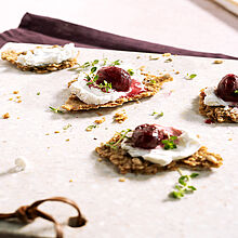 Cracker belegt mit Ziegenkäse und einem Topping aus Ofentrauben, beträufelt mit Honig. Serviert auf einer grauen Schieferplatte