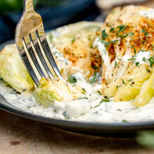 Auf dem Teller liegen geröstete Weißkohlstücke in einer cremigen Kräuter-Käsesoße. Eine Gabel nimmt gerade ein Stück des goldbraun gebratenen Kohls auf. Das Gericht wirkt frisch, würzig und appetitlich angerichtet.