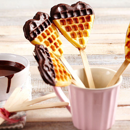 Pfiffige Waffeln am Stiel aus dem Waffeleisen mit Schokoglasur in einem Kaffeebecher präsentiert.