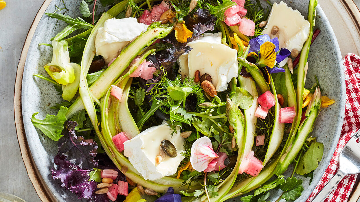 Frühlingsfrischer Rhabarber-Spargel-Salat mit Camembert Ein frischer Rhabarber-Spargel-Salat mit Wildkräutern, garniert mit Camembert, serviert auf einem rustikalen Salatteller.