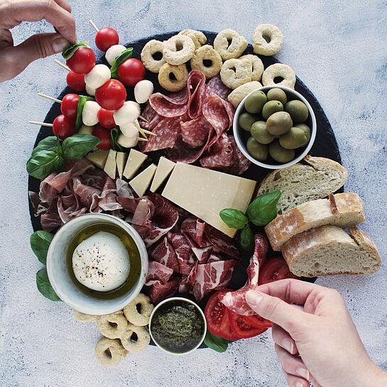 Italienisches Charcuterie Board mit Grana Padano, Parmaschinken, Coppa, Kirschtomaten, Oliven und Basilikumpesto.