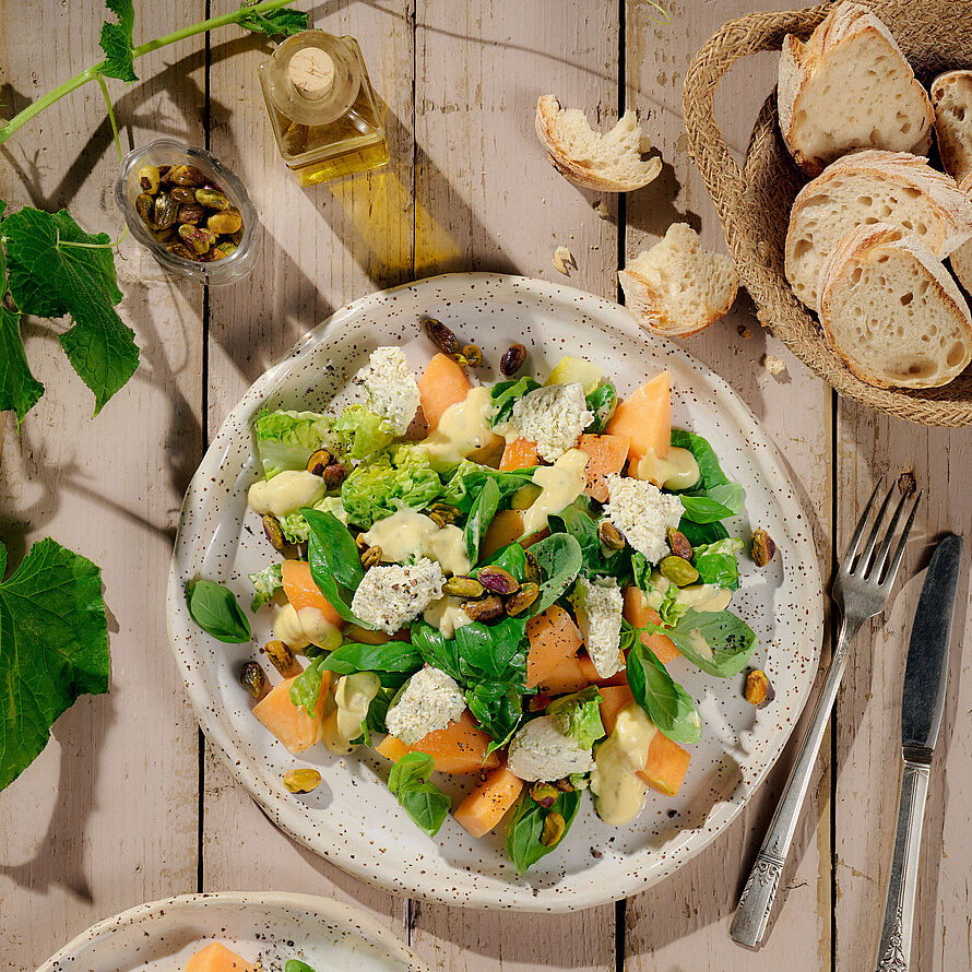 Wunderbarer Sommersalat auf einem runden Teller serviert mit Melone, Basilikum und BRESSO feine Kräuter
