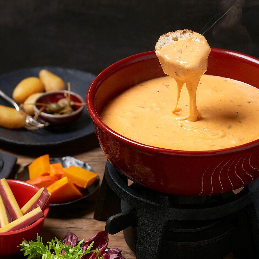 Käsefondue, zubereitet aus einer Mischung von drei Käsesorten, angereichert mit Tomatenstückchen und serviert mit Kartoffeln.