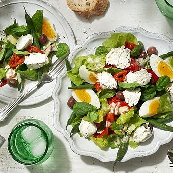 Unser Salat Nizza besteht aus frischen grünen Blattsalaten, Tomaten, grünen Bohnen, Eiern und Oliven, die mit Thunfisch und einer leichten Vinaigrette serviert werden