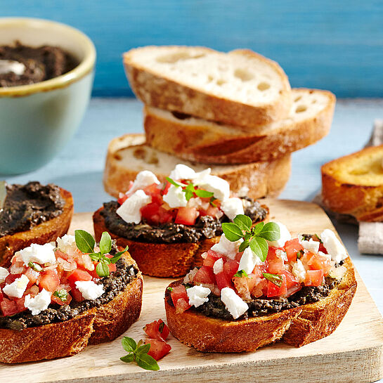 Gebackene Baguettescheiben mit Tapenade, frischen Tomaten und Chavroux Ziegenkäse. Garniert mit Tymian und Bailikum