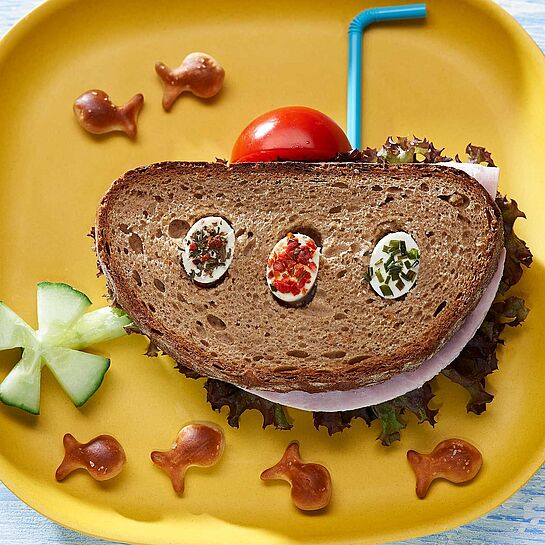 Pfiffiges Pausenbrot als lustiges U-Boot serviert mit Tomate, Gurke und Fischbrezeln