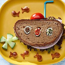 Pfiffiges Pausenbrot als lustiges U-Boot serviert mit Tomate, Gurke und Fischbrezeln