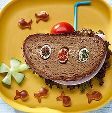 Pfiffiges Pausenbrot als lustiges U-Boot serviert mit Tomate, Gurke und Fischbrezeln