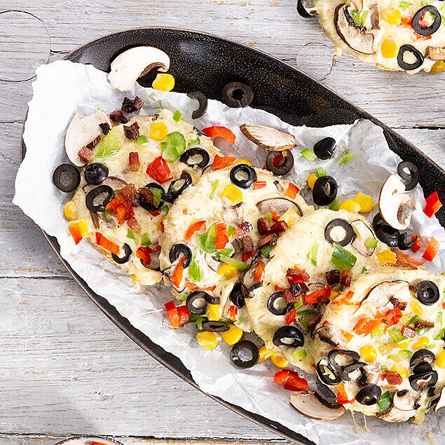 Ovale schwarze Schale mit heißen Pizzabrötchen nach mexikanischer Art. Als Beilage ein Schälchen mit Mais