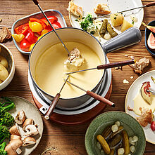 Schön angerichtetes Käsefondue ohne Alkohol mit zahlreichen Zutaten in kleinen Schälchen. Dazu frisches Brot.