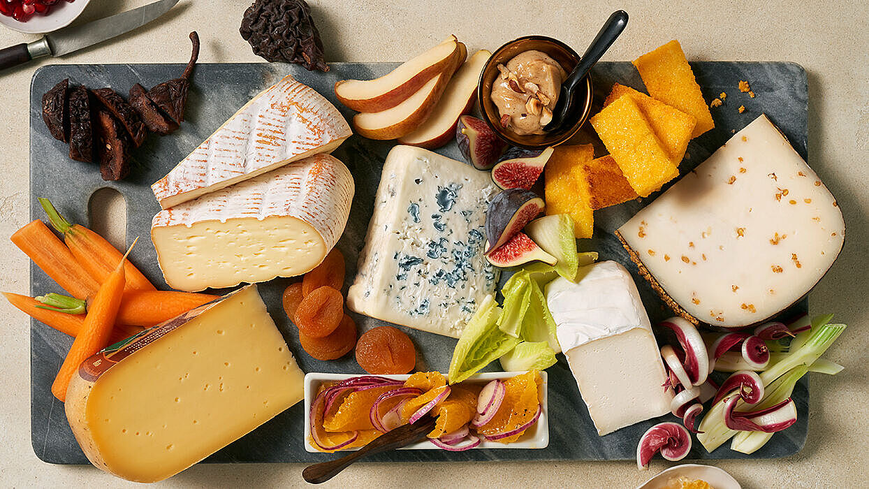 Diverse Käsesorten angerichtet auf einem Board mit frischem Obst und knackigen Gemüse