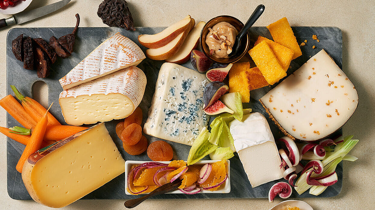 Diverse Käsesorten angerichtet auf einem Board mit frischem Obst und knackigen Gemüse