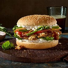 Pulled Blumenkohl Burger mit würziger Barbecuesauce, frischem Romanasalat, Apfel, Tomate, Avocado und cremigem Bresso. Serviert auf einem Holzbrett.