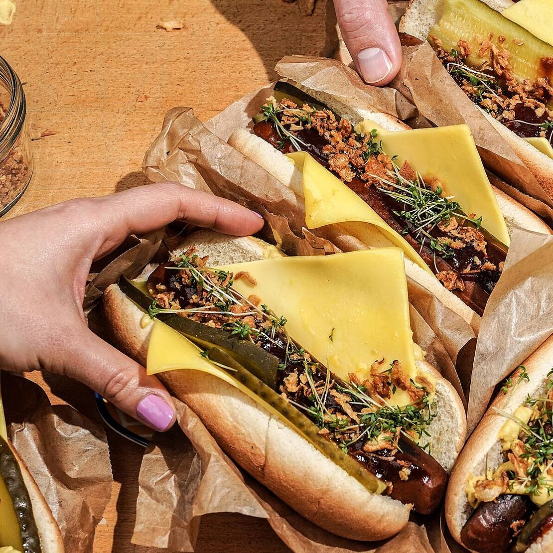 Vegane Hot Dogs mit Hope Scheibenkäse, Tofuwürstchen und Gewürzgurken, serviert auf einem großen verzierten Teller. 