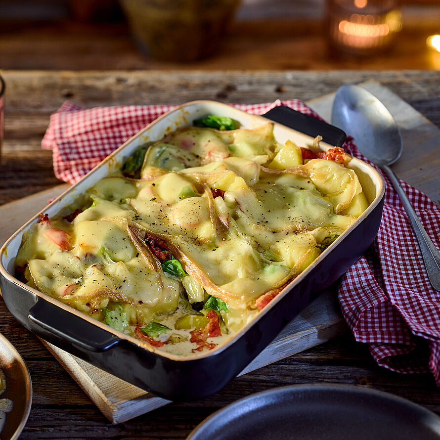 Spitzkohlgratin mit Speck, Kartoffeln und Raclette-Käse, perfekt überbacken für ein herzhaftes und wärmendes Gericht. Serviert in einer Auflaufform. 