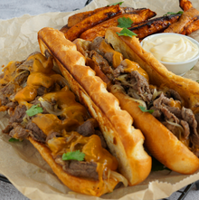 Philly Cheesesteak Sandwich mit dünn geschnittenem Ribeye-Steak, geschmolzenem Cheddar und Zwiebeln im knusprigen Brioche-Baguette.