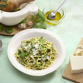 Spaghetti Pesto Verde mit geriebenen Parmesan und ganzen Basilikumblättern. Dazu eine Schüssel mit Pinienkernen