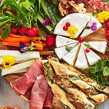 Verschiedene Gemüsesorten wie Möhren, Kirschtomaten, Radieschen+ Schinken und Käse auf einem Charcuterie Board
