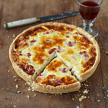 Angeschnittene Quiche Lorraine auf einem Holzteller. Klassische französische Küche. 