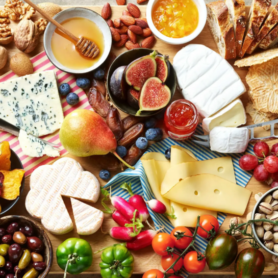 Farbenfrohes deluxe Käseboard mit cremigem Käse Variationen, saftigen Trauben, Nüssen, Oliven & Chutneys auf rustikalem Holzbrett, ideal für einen geselligen Abend.