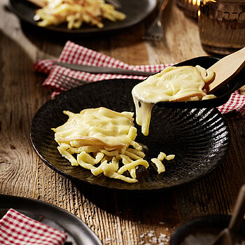 Eine schnelle und einfache winterliche Mahlzeit. Spätzle überbacken mit Raclette-Käse auf einem schwarzen Teller serviert.