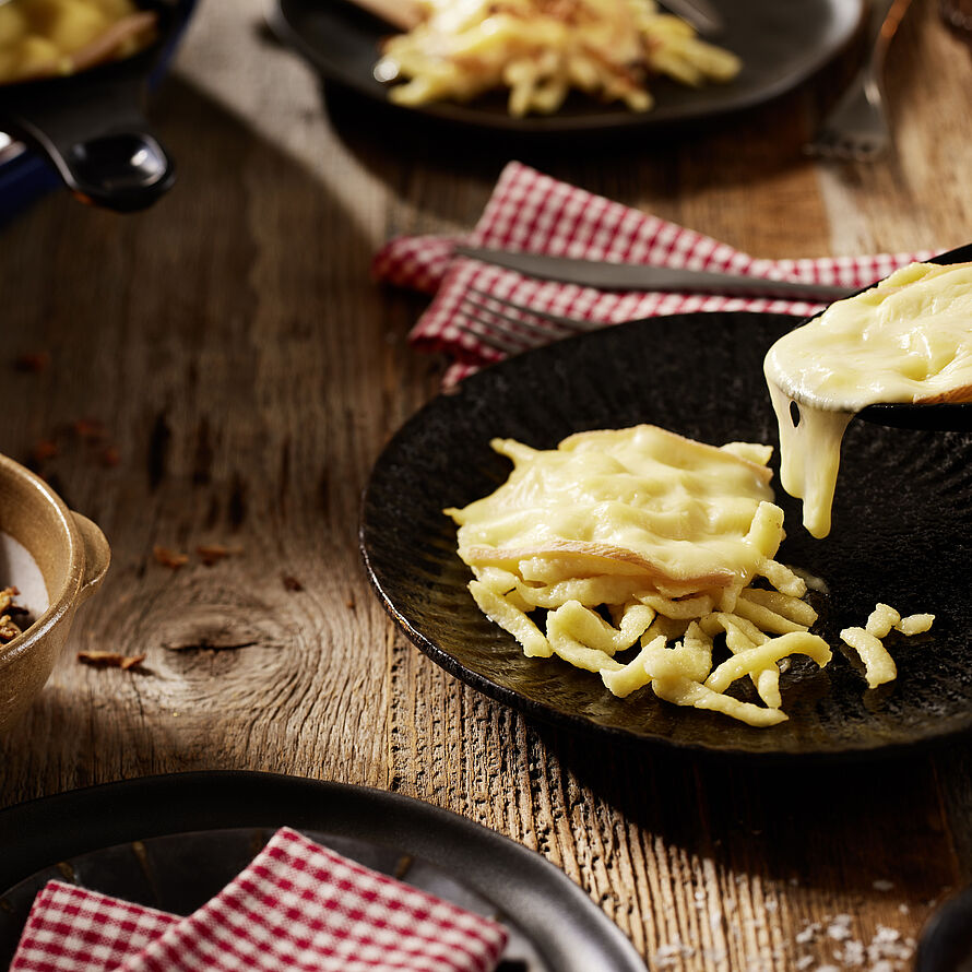 Eine schnelle und einfache winterliche Mahlzeit. Spätzle überbacken mit Raclette-Käse auf einem schwarzen Teller serviert. 