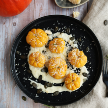 Schwarzer Teller mit kleinen Kürbisgnocchi in Kürbisform, serviert auf cremiger Käsesoße, garniert mit geriebenem Käse und Kürbiskernen.