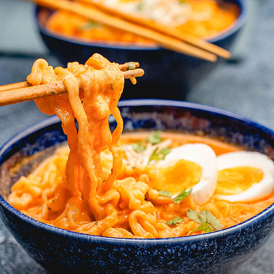 Ramen Carbonara Rezept mit cremiger Cheddar-Soße, garniert mit frischem Koriander und einem halbierten Ei in einer Schüssel angerichtet.