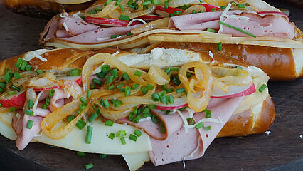Bayerischer Hot Dog mit saftigem Leberkäse, cremigem Käse, süßem Senf und knackigen Radieschen auf knuspriger Laugenstange.