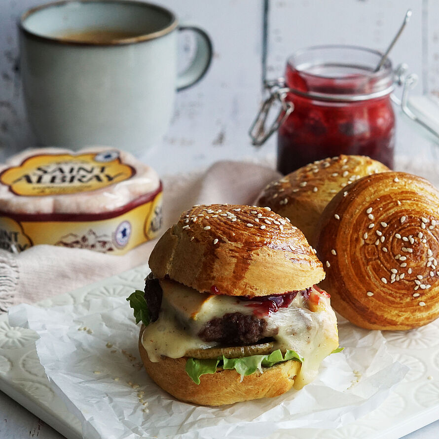 Croissant Burger mit saftigem Patty, cremigem Saint Albray Käse, karamellisierter Birne und frischem Salat auf einem Teller serviert.