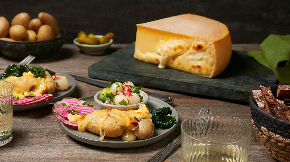 Kartoffeln mit Käse überbacken und ein Raclette Käse am Stück auf einer schwarzen Schieferplatte. 