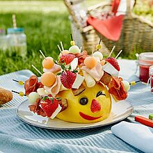 Käseigel Gérard hat auf seinen Spießen Géramont, Honigmelone und Putenbrust und sitzt auf einer Picknickdecke