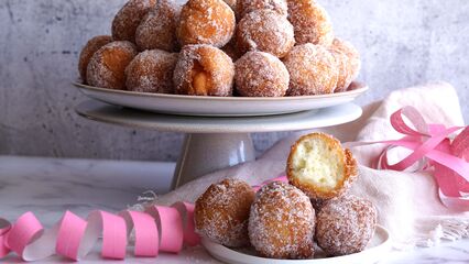 Frisch frittierte Quarkbällchen bestäubt mit feinem Zucker auf einer weißen Kuchenplatte und einem Teller serviert. 