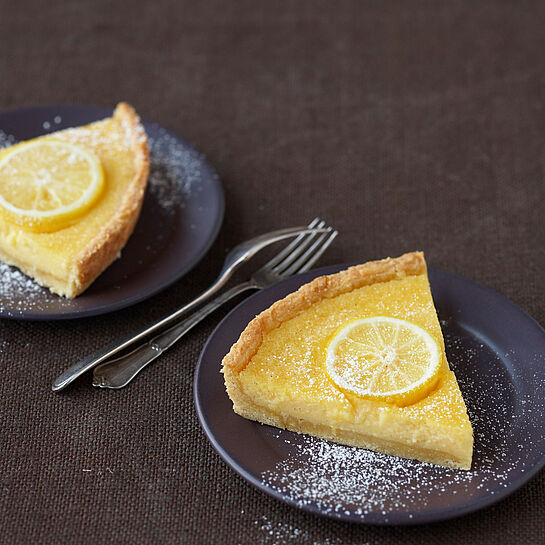 Tarte au citron mit Puderzucker bestreut und einer Zitronenscheibe garniert