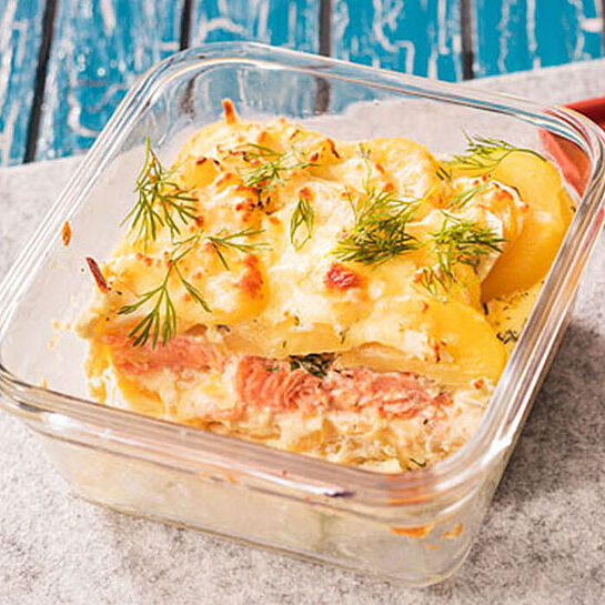 Durchsichtige Auflaufform mit Kartoffel-Lachs-Gratin. Garniert mit frischem Dill und goldbraun gebacken.