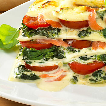 Köstliches Stück Spinat-Tomaten-Lasagne mit frischen Zutaten und schmackhaft verlaufendem Käse. Serviert auf einem weißen Essteller. 