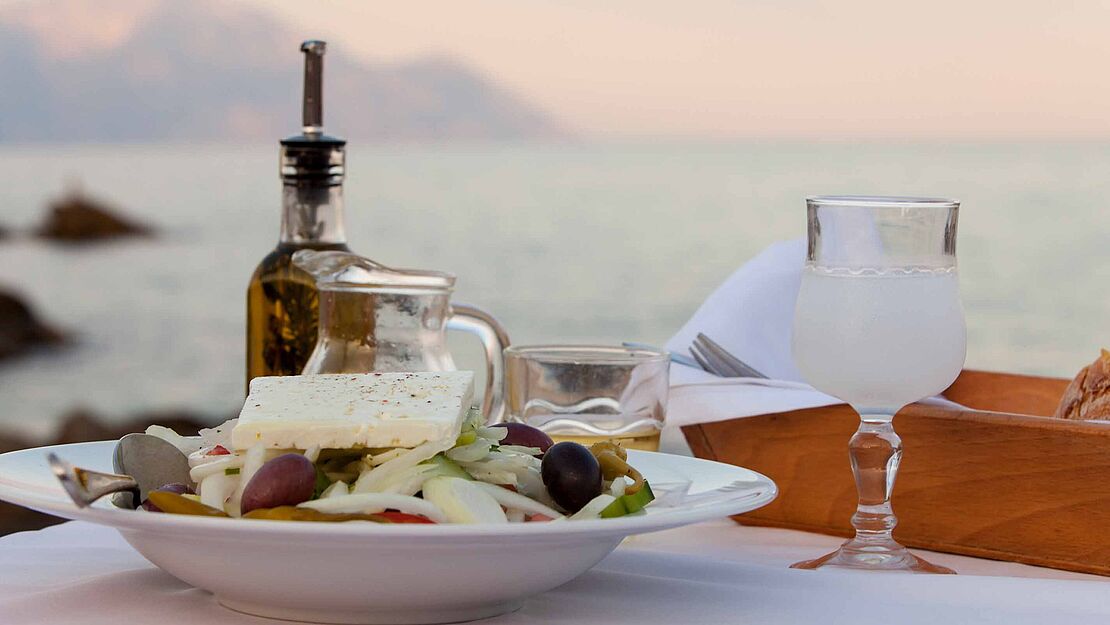 Fein hergerichteter Tisch in der Abendsonne mit einem Fetasalat, frischem Brot und Olivenöl