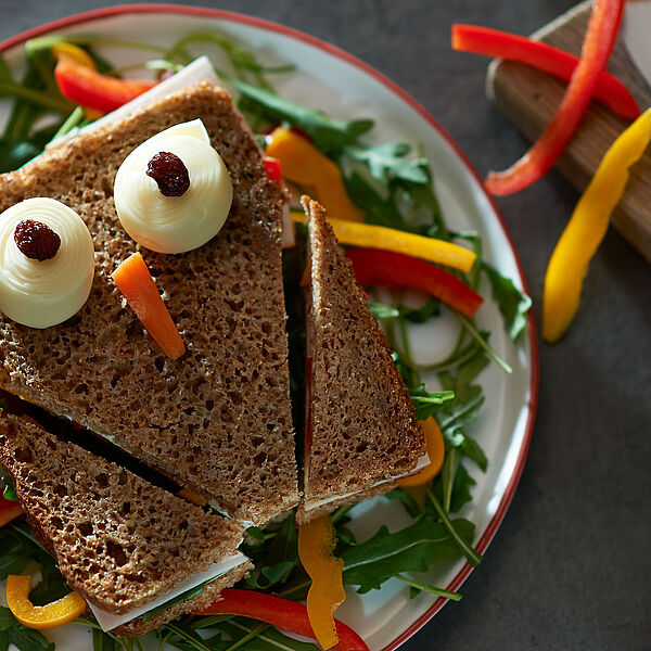 Kindliches Vollkorn-Pausenbrot mit einem drapierten Gesicht aus Käse, Karotten und Rosinen