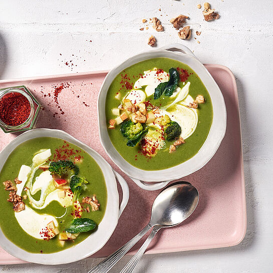 Tablet mit zwei Portionen grüner Gemüsesuppe in mittleren Schüsseln garniert mit Brunch Frischkäse und knackigen Walnusskernhälften