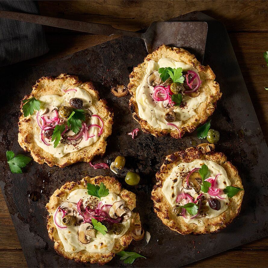 Kleine Pizzen mit Blumenkohl und einem cremigen Belag aus Brunch, marinierten Zwiebeln, frischen Champignons und Oliven, verfeinert mit Petersilie.