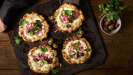 Kleine Pizzen mit Blumenkohl und einem cremigen Belag aus Brunch, marinierten Zwiebeln, frischen Champignons und Oliven, verfeinert mit Petersilie.