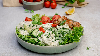 Eine griechische Bowl mit frischem grünen Salat, Gurken, Tomaten und knusprig gebratenen Hähnchen-Hackbällchen, getoppt mit BRESSO Frischkäse.